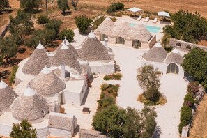 A cluster of traditional stone-roofed buildings with a swimming pool and lounge chairs. - Masseria Ferrari – A Trulli Village with Private Pool in the Heart of the Itria Valley (Pozzo Salerno)