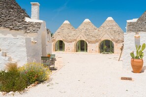 A building with three conical roofs, a gravel courtyard, and a cactus plant. - Masseria Ferrari – A Trulli Village with Private Pool in the Heart of the Itria Valley (Pozzo Salerno)