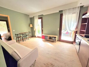 Un salon avec un canapé, une table à manger avec des chaises, un banc et un coin cuisine équipé d’une cuisinière.