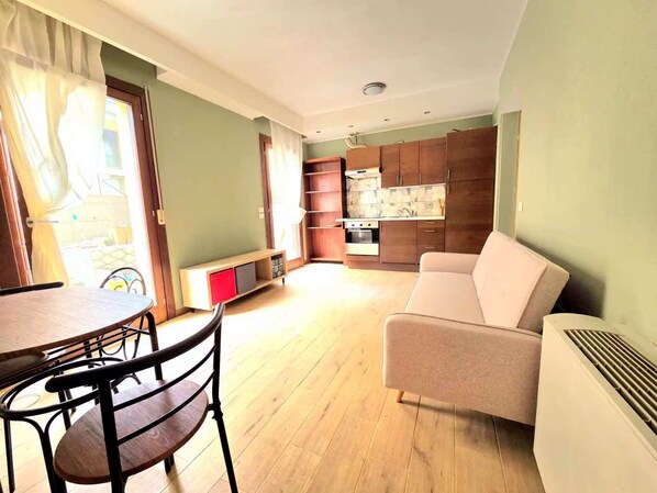 Un salon comprenant un canapé, une table à manger avec des chaises, un coin cuisine avec des placards et un petit espace détente avec un banc.