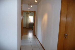 Un pasillo estrecho con una puerta de madera a la derecha y una ventana con cortinas al fondo.