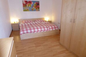Ein Schlafzimmer mit karierter Bettdecke, zwei Nachttischlampen, einem Holzschrank und einem floralen Gemälde an der Wand.