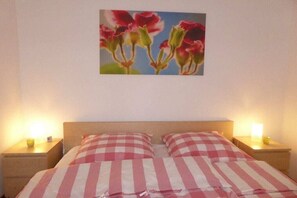 Una cama con ropa de cama a cuadros, una mesita de noche con una lámpara y un cuadro de flores en la pared.