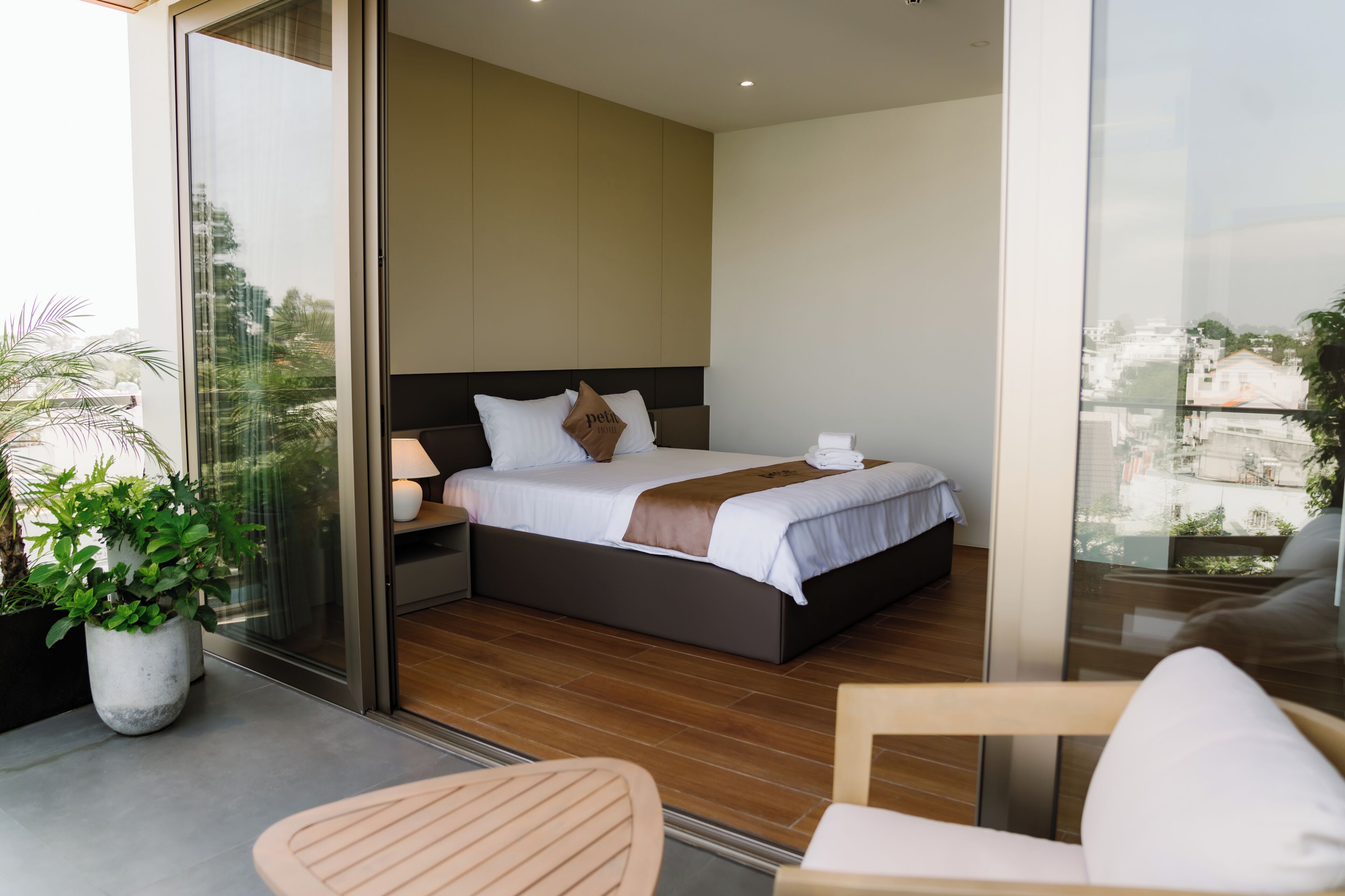 A modern hotel room with a large bed, a bedside table, a lamp, and a view through a glass door.