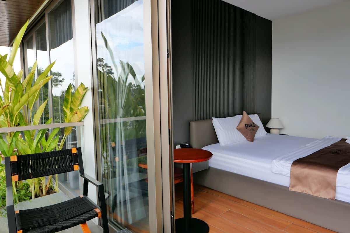 Une chambre d’hôtel moderne, équipée d’un lit, d’une petite table ronde, d’une chaise et d’une grande fenêtre donnant sur un paysage verdoyant.