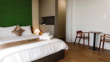 Una habitación de hotel con cama, cabecera verde, televisor montado en la pared, una pequeña mesa con sillas y una lámpara.
