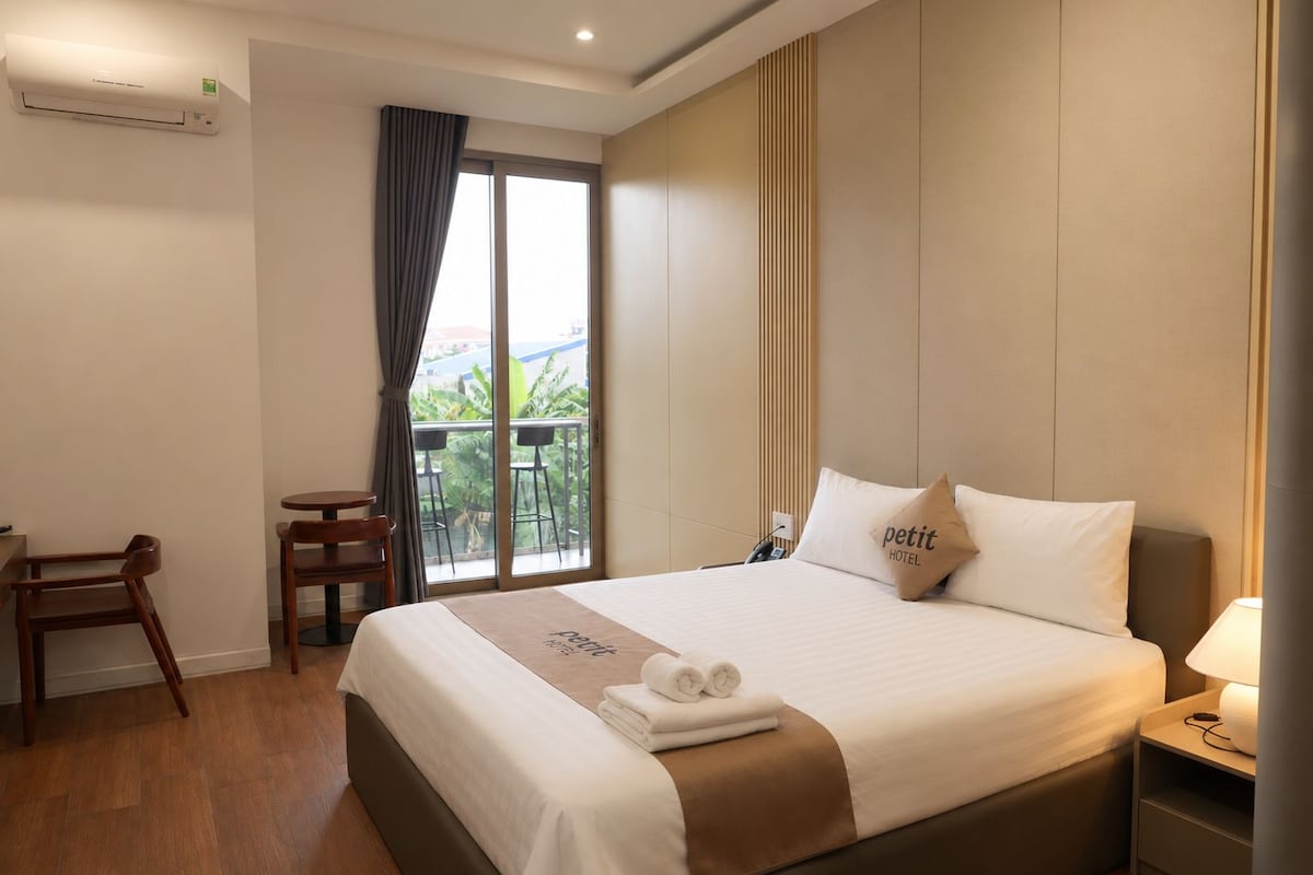 Habitación de hotel con cama, escritorio, silla, ventana con cortinas y balcón.