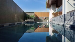 A modern pool area with clear water, wooden and concrete walls, and potted plants.
