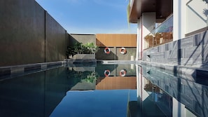 Un área de piscina moderna con agua cristalina, paredes de madera y hormigón, y plantas en macetas.