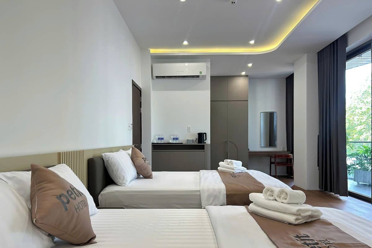 Une chambre d’hôtel avec deux lits, un bureau, un miroir et une vue sur la verdure environnante.