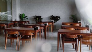 A spacious dining area with wooden tables and chairs, potted plants, and a modern wall design.
