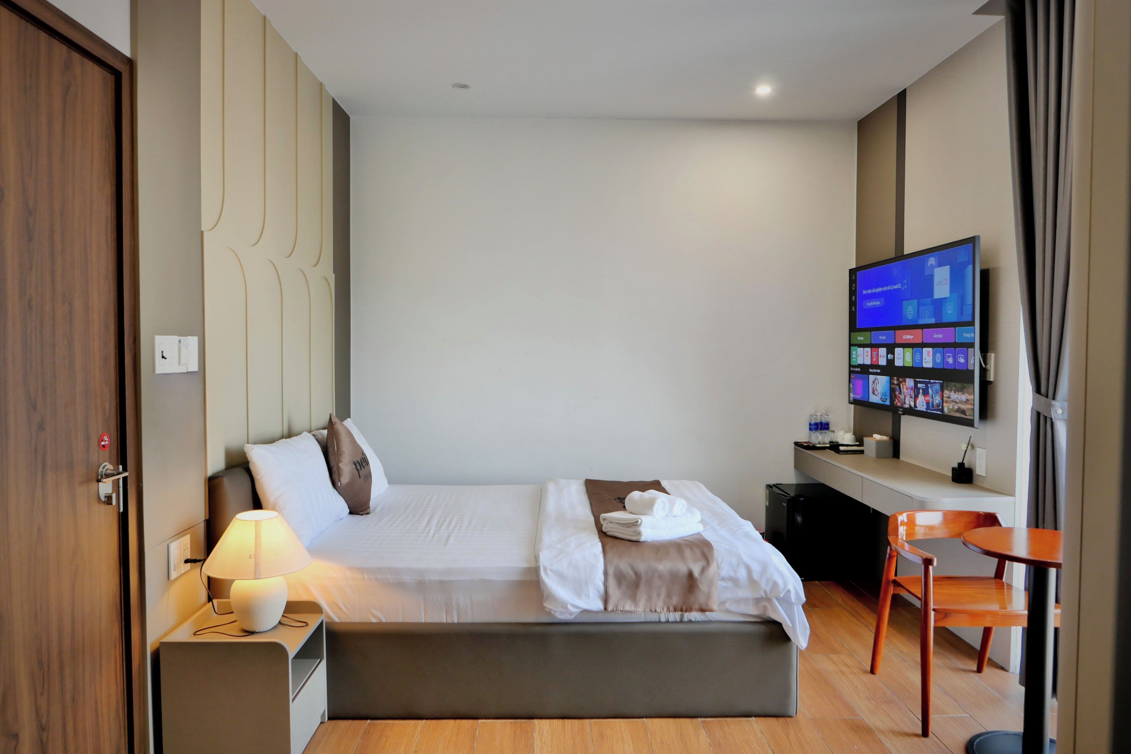Ein Hotelzimmer mit Bett, Nachttisch, Lampe, Fernseher und einem kleinen Tisch mit Stühlen.