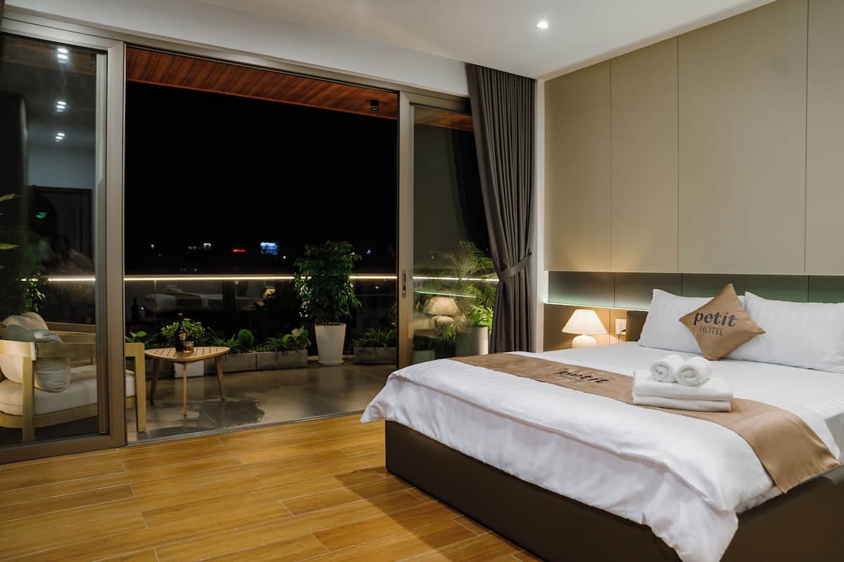 Une chambre d’hôtel moderne avec un grand lit, une petite table, un canapé et un balcon agrémenté de plantes.