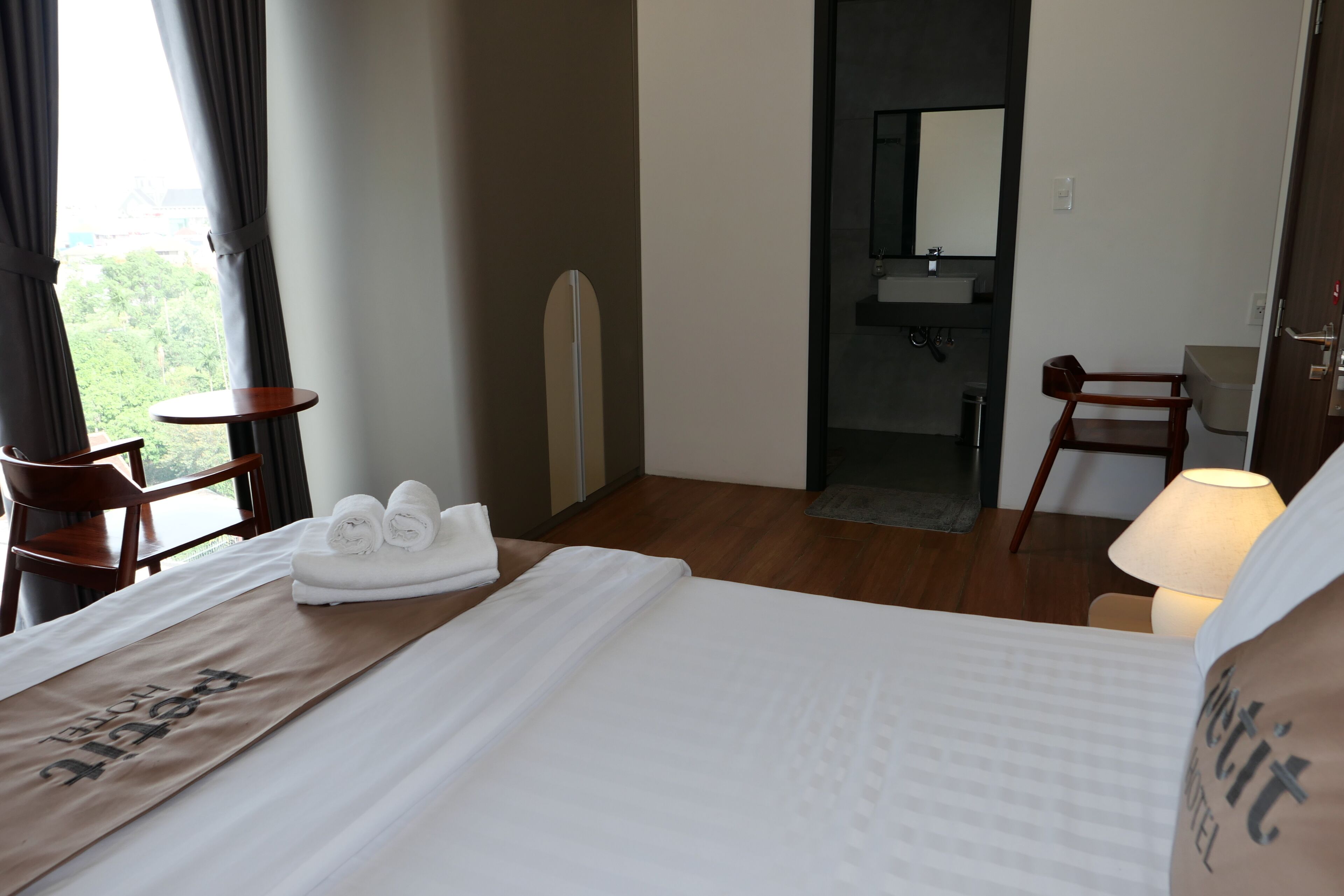 Habitación de hotel con cama, escritorio, silla, baño y vista a zonas verdes.