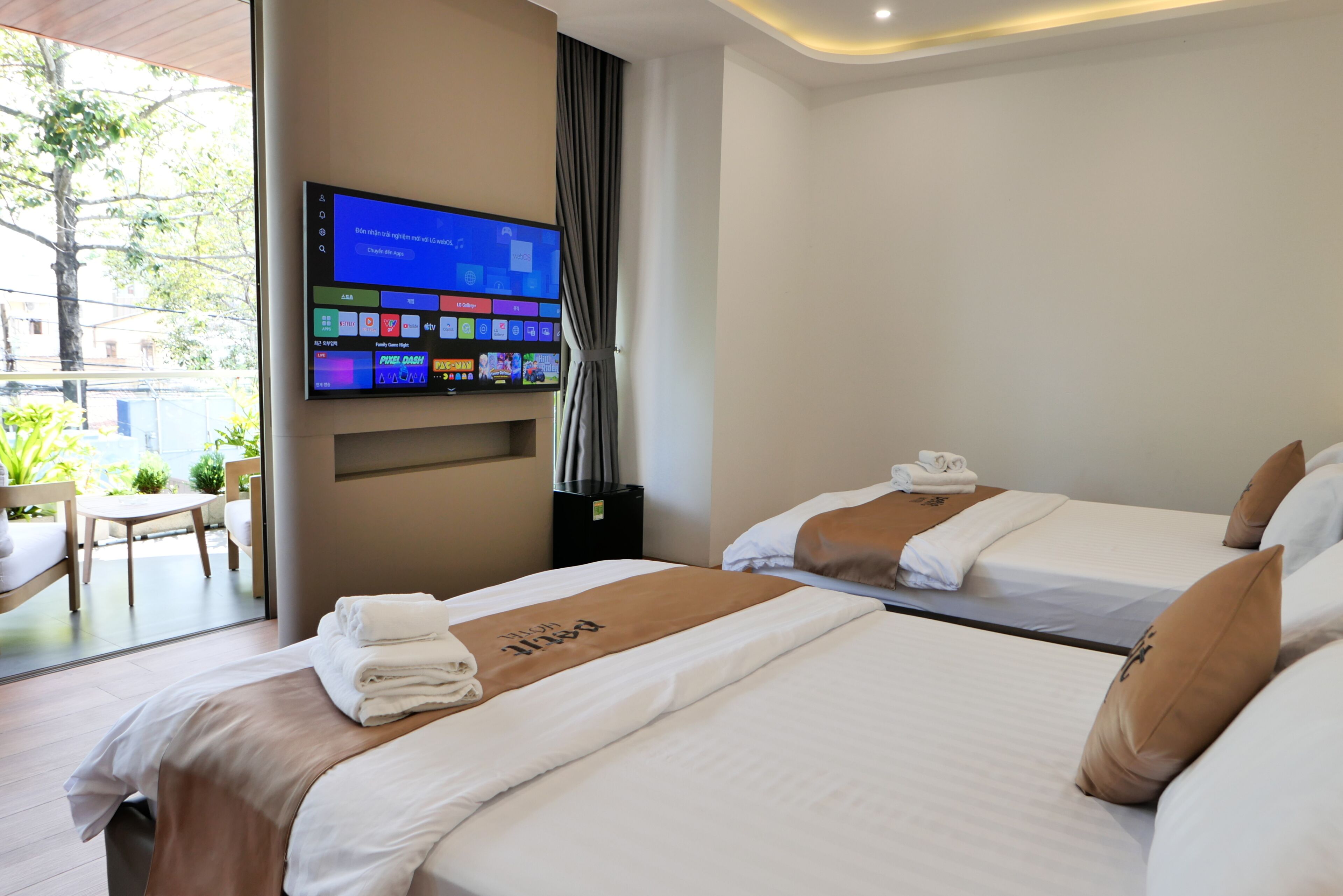 Een hotelkamer met twee bedden, een wandtelevisie en uitzicht op het buiten.