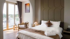 A hotel room with a bed, a chair, a nightstand, a lamp, and a view through a large window.