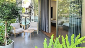 Una sala de estar moderna con un ventanal que da a un balcón, una mesa de madera, dos sofás blancos y diversas plantas de interior.