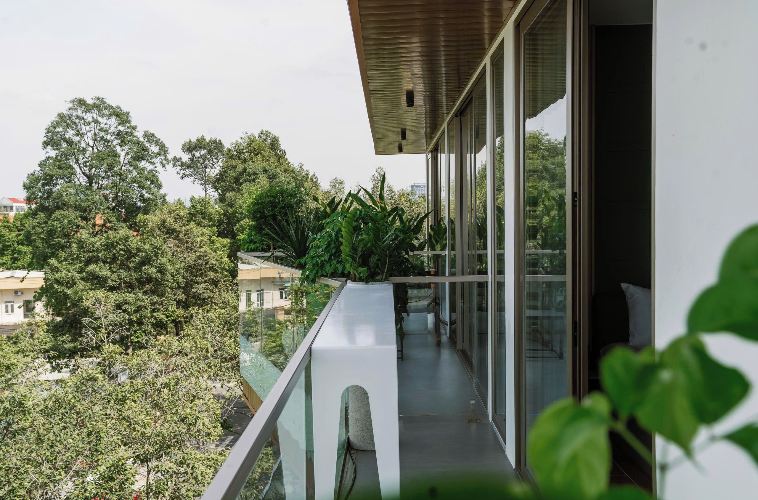 A modern balcony with glass railings, a view of trees, and a glimpse of the interior.