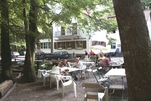 Ein Straßencafé mit Tischen und Stühlen, im Hintergrund ein Gebäude mit der Aufschrift 'Sturmundthaus Edeenkoben' und Bäume, die die Umgebung säumen.