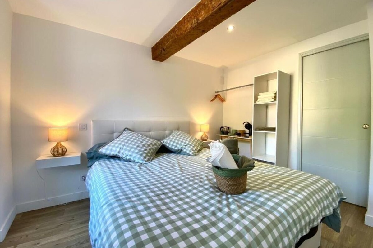 Een slaapkamer met een geruit sprei, bedlampen, een houten balk in het plafond, een kledingkast en een mand met een handdoek.