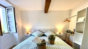 Ein Schlafzimmer mit karierter Bettdecke, zwei Nachttischlampen, einer Pendelleuchte, einem Kleiderschrank und einem Fenster mit Jalousien.