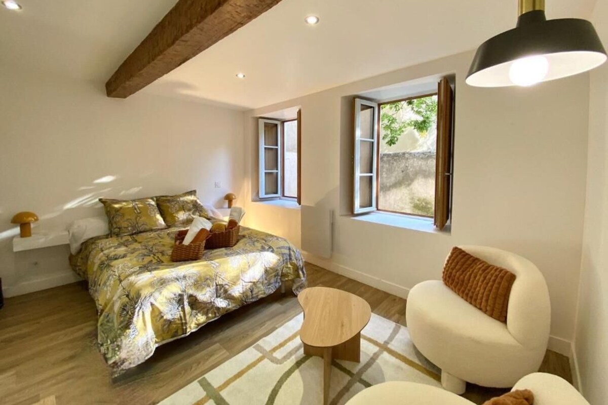 Een slaapkamer met een bed, een klein tafeltje, een bank en een raam met gordijnen.