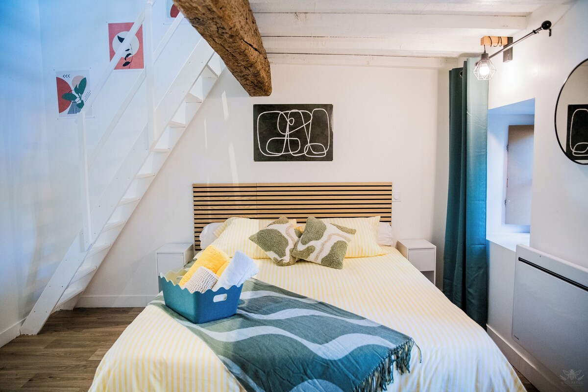 Een slaapkamer met een bed, een houten hoofdbord, een klein nachtkastje, een nachtlampje, een spiegel en een trap.
