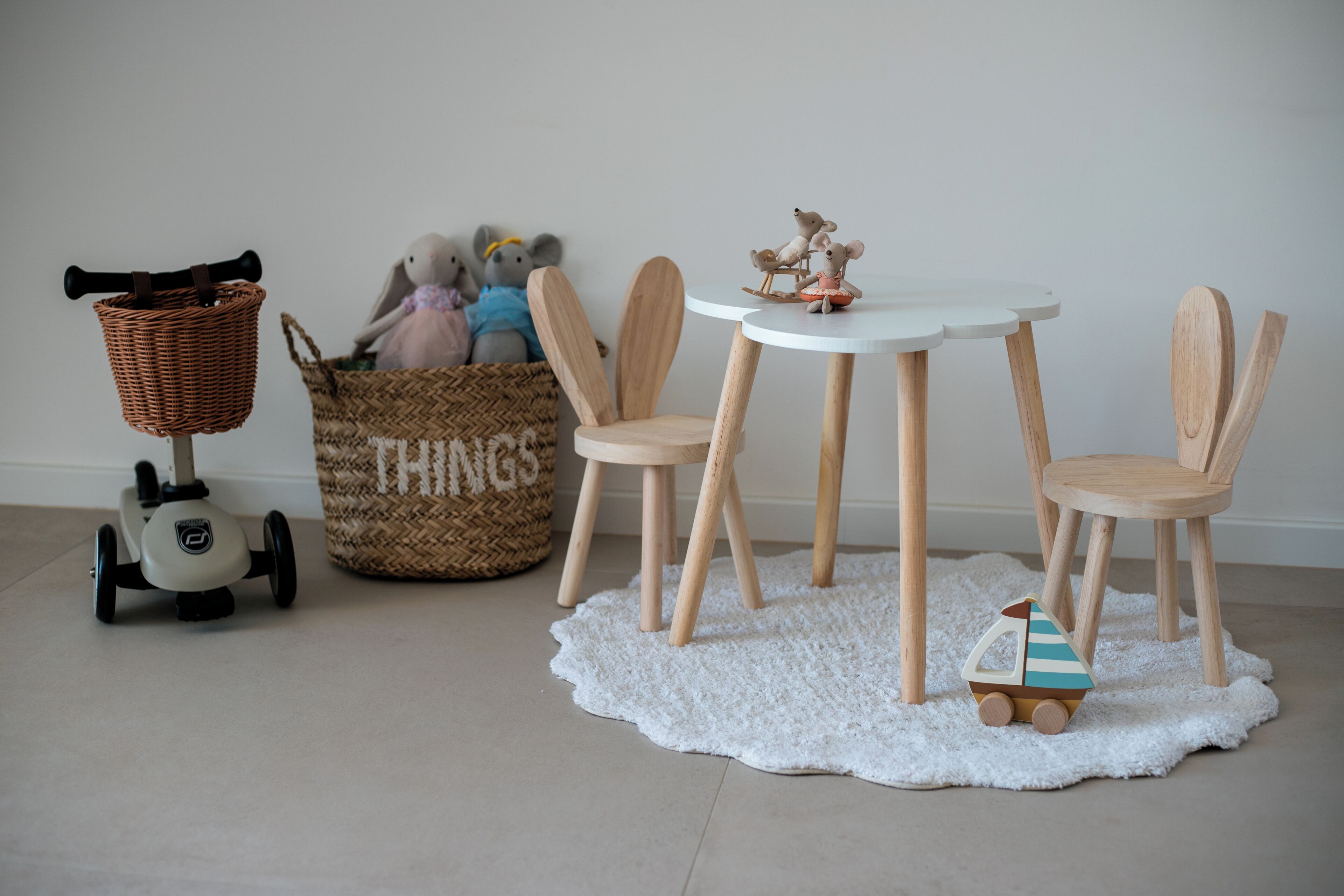 Een kamer met een ronde witte tafel, vier houten stoelen, een rieten mand, een gevlochten mand met de tekst 'THINGS', een klein bootje en een scooter.