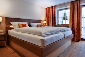 Ein Hotelzimmer mit einem großen Bett, einem Holzkopfende, zwei Nachttischen und einem Fenster mit Vorhängen.