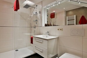 Ein modernes Badezimmer mit Duschkabine aus Glas, einem weißen Waschbecken und einem großen Spiegel.