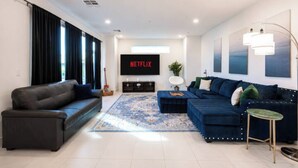 Un salon moderne avec un canapé, une table basse, un téléviseur et un tapis.