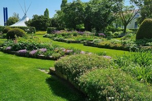 Un jardin bien entretenu, agrémenté de différents parterres de fleurs et, au fond, d’une structure blanche remarquable.