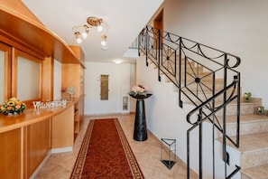 A reception area with a wooden counter, a black vase with flowers, a staircase with black railings, and a red carpet. - Holiday apartment with 1 bedroom (Bad Füssing)