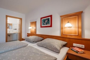 A hotel room with two beds, a wooden headboard, bedside lamps, a framed picture, and a nightstand with books. - Holiday apartment with 1 bedroom (Bad Füssing)