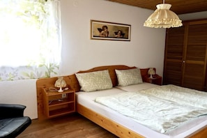 Ein Schlafzimmer mit einem hölzernen Bett, einem Nachttisch, einer Lampe, einem gerahmten Bild an der Wand und einem Fenster mit Vorhängen.