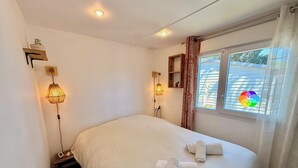 Een net opgemaakt bed met opgerolde handdoeken, een bedlamp en een raam met gordijnen.