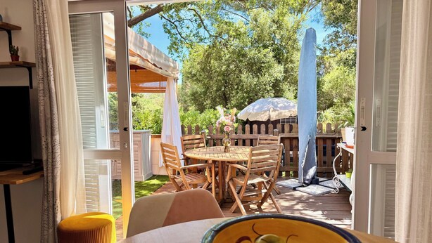 Een open deur die leidt naar een terras met een houten tafel, stoelen en een eethoek.