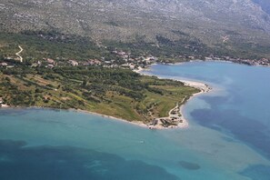 Eine Luftaufnahme einer Küstenregion mit Strand, einer kleinen Siedlung und hügeligem Gelände.