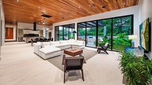 A modern living room with a large sectional sofa, a coffee table, and a dining area with a kitchen in the background. - Casa Ventura Luxury Villa Golondrinas Hacienda Pinilla Costa Rica (Tamarindo)