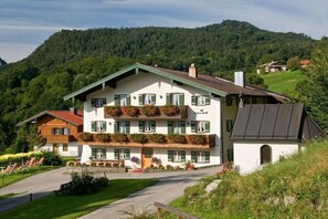 Ein mehrstöckiges Hotel mit Gründach, Balkonen mit Blumenkästen und einer Bergkulisse.