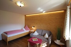 Ein Zimmer mit einem Bett, einem Schlafsofa, einem kleinen Tisch, einer Lampe und einer Zimmerpflanze.
