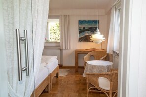 Ein kleines Zimmer mit einem Bett, einem Tisch mit Stühlen, einem Bild an der Wand und einer Hängeleuchte.
