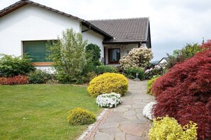 Ein Haus mit einem gepflasterten Weg zum Eingang, umgeben von Sträuchern und einem gepflegten Rasen.