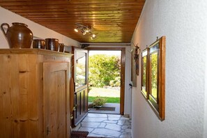 Ein Holzboden mit Steinbelag führt zu einer offenen Tür, ein Holzschrank mit Tonwaren und gerahmte Bilder an der Wand.