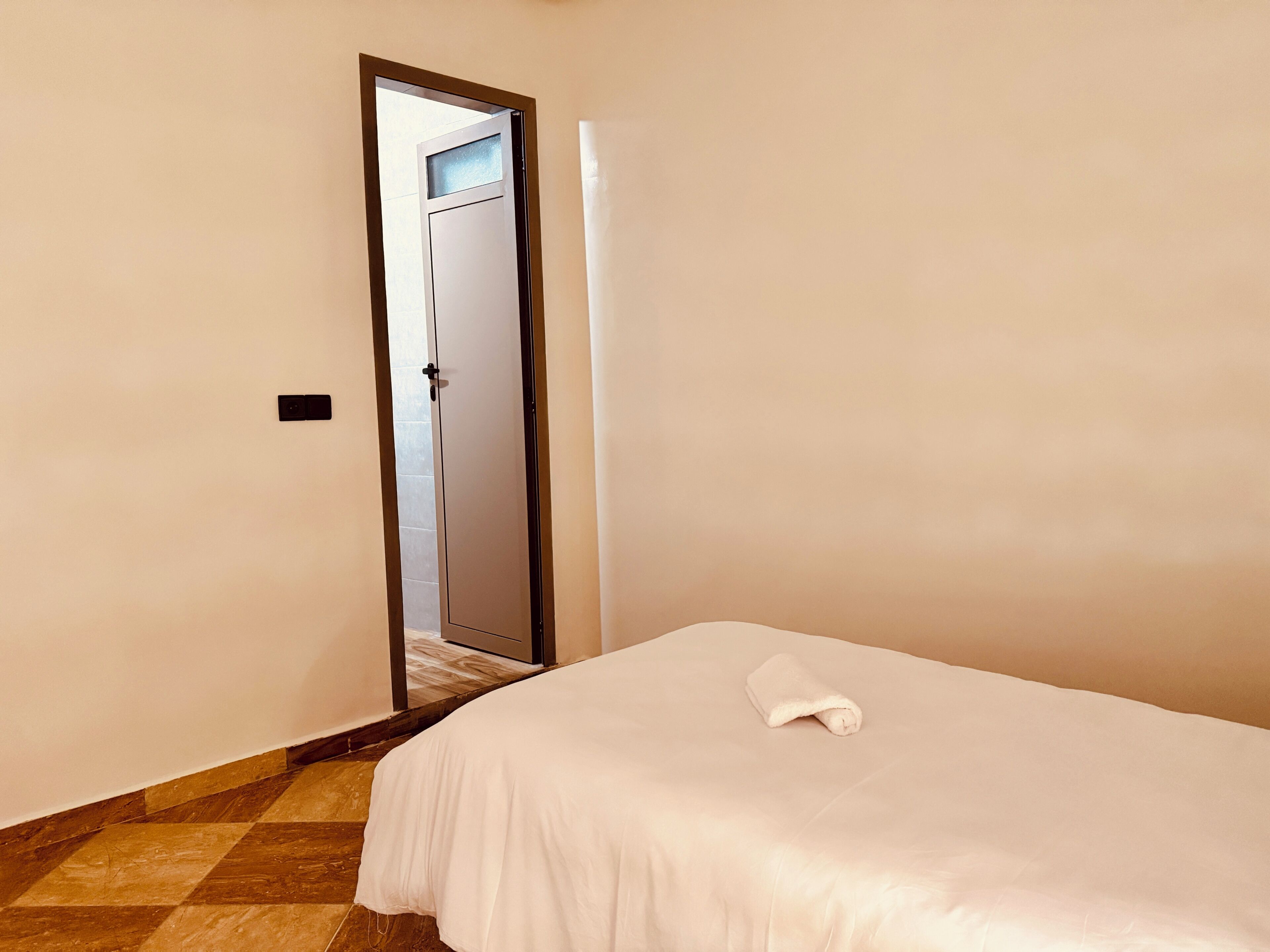 A hotel room with a bed, a door, and a tiled floor.
