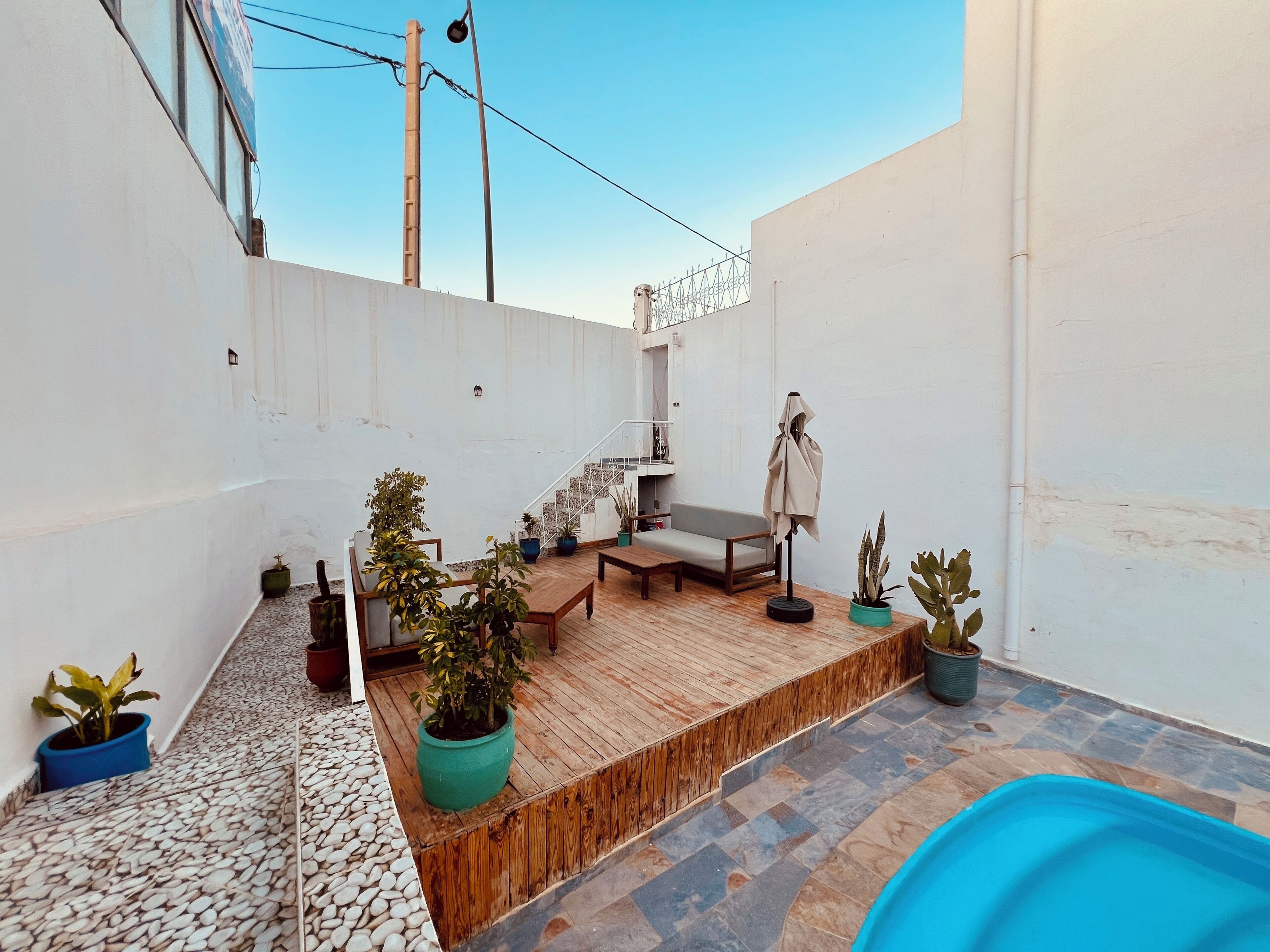A rooftop patio with a pool, wooden deck, potted plants, a sofa, and a staircase.