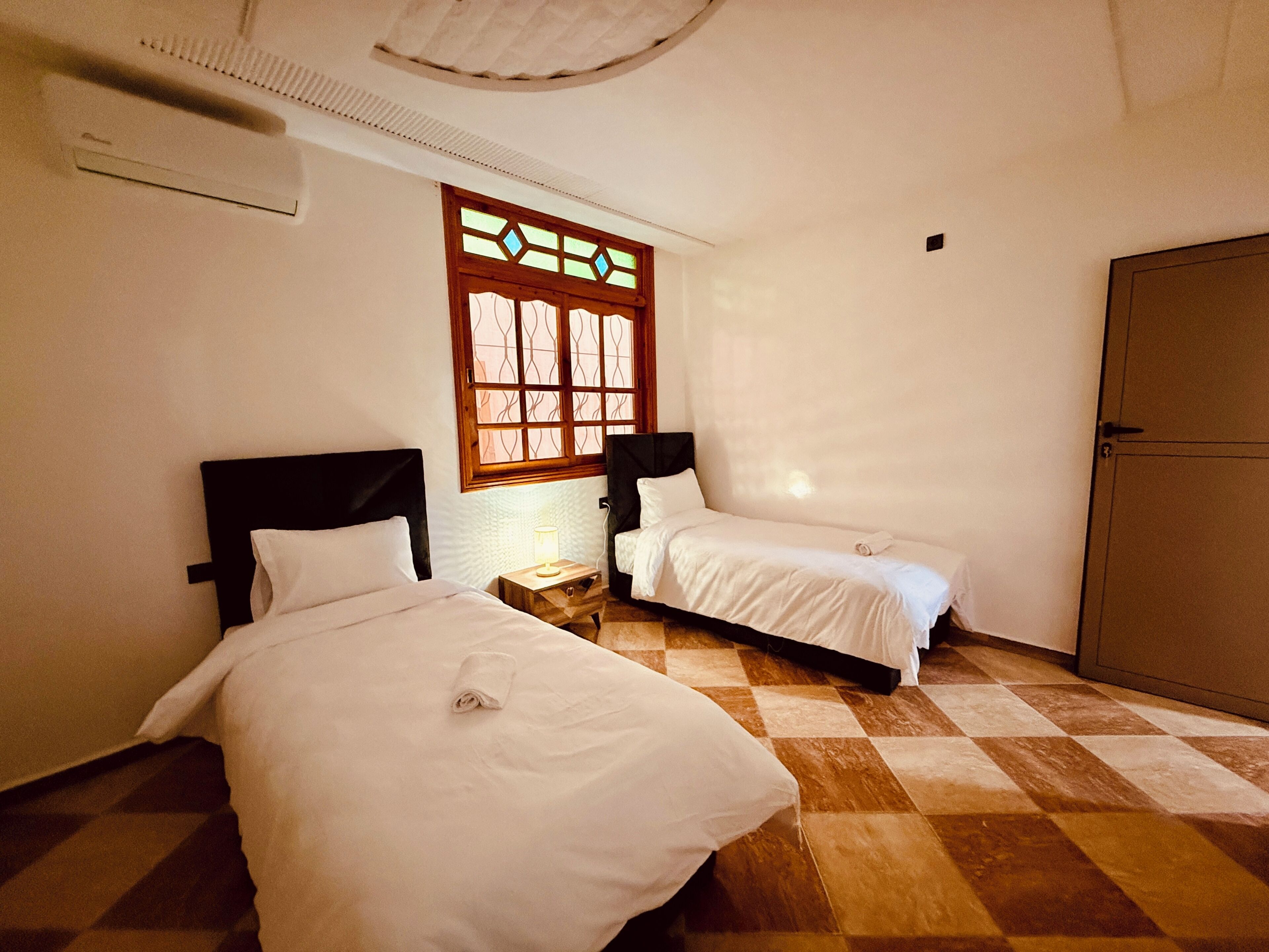 A room with two beds, a window with stained glass, a wooden floor, and a wardrobe.