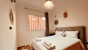 Um quarto com uma cama, uma janela com grades, um relógio de parede e um lustre.