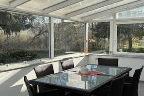 Ein Wintergarten mit Glastisch und Korbstühlen, umgeben von großen Fenstern.