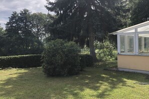 Ein Wintergarten mit Glasdach, umgeben von gepflegtem Rasen und üppigem Grün.